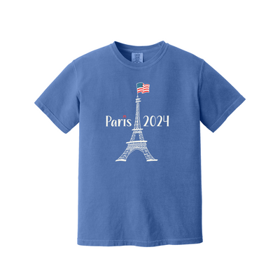 A blue short-sleeve crewneck t-shirt featuring a white Eiffel Tower graphic with 'Paris 2024' text and a small French flag on top, displayed on a solid white background.